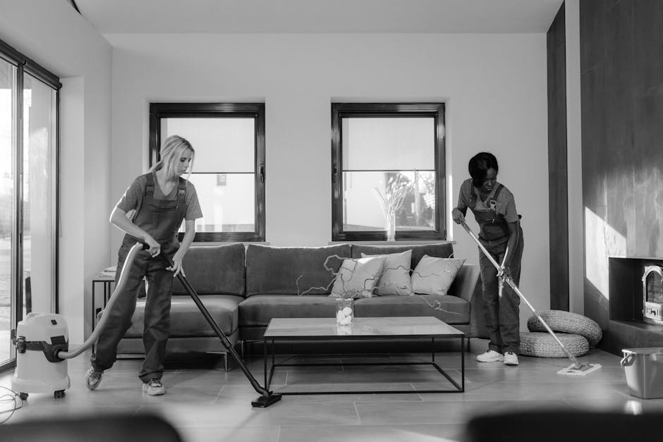 Interior view of a modern kitchen with three professional cleaners from Hammersmith Cleaner, engaged in surface cleaning and sanitisation. One cleaner is standing on a step stool on the kitchen counte